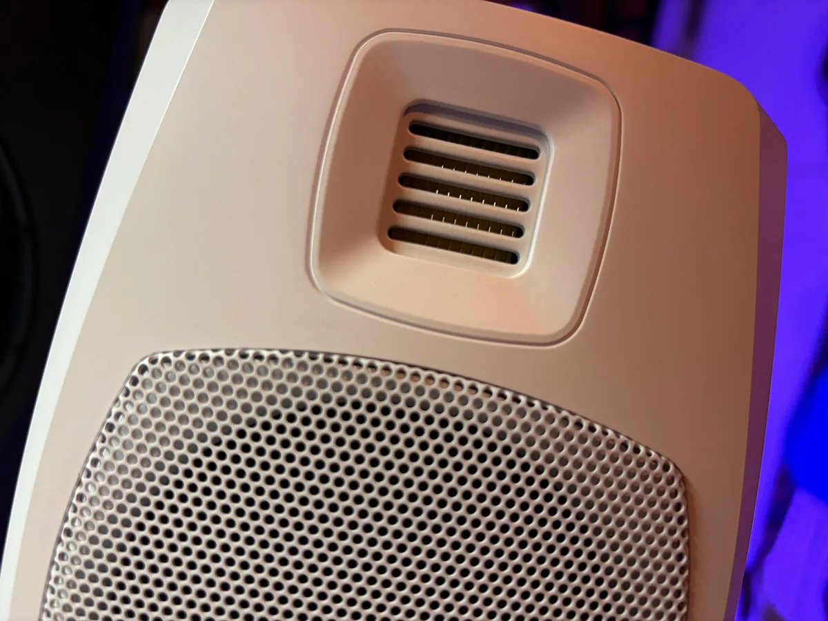 A close-up of an ADAM Audio studio monitor, showing its ribbon tweeter port and perforated woofer grille, lit in purple studio light.